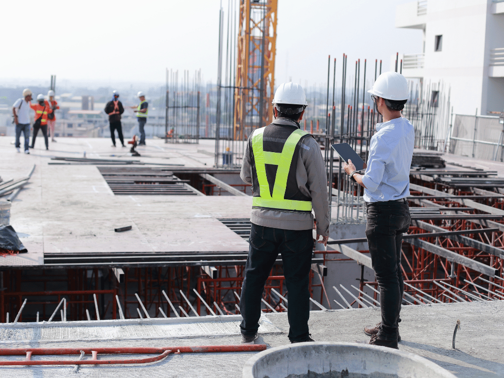 Arna Constructions site supervisor and engineer in safety gear discussing project progress on a tablet at a high-rise building construction site in Greater Noida.