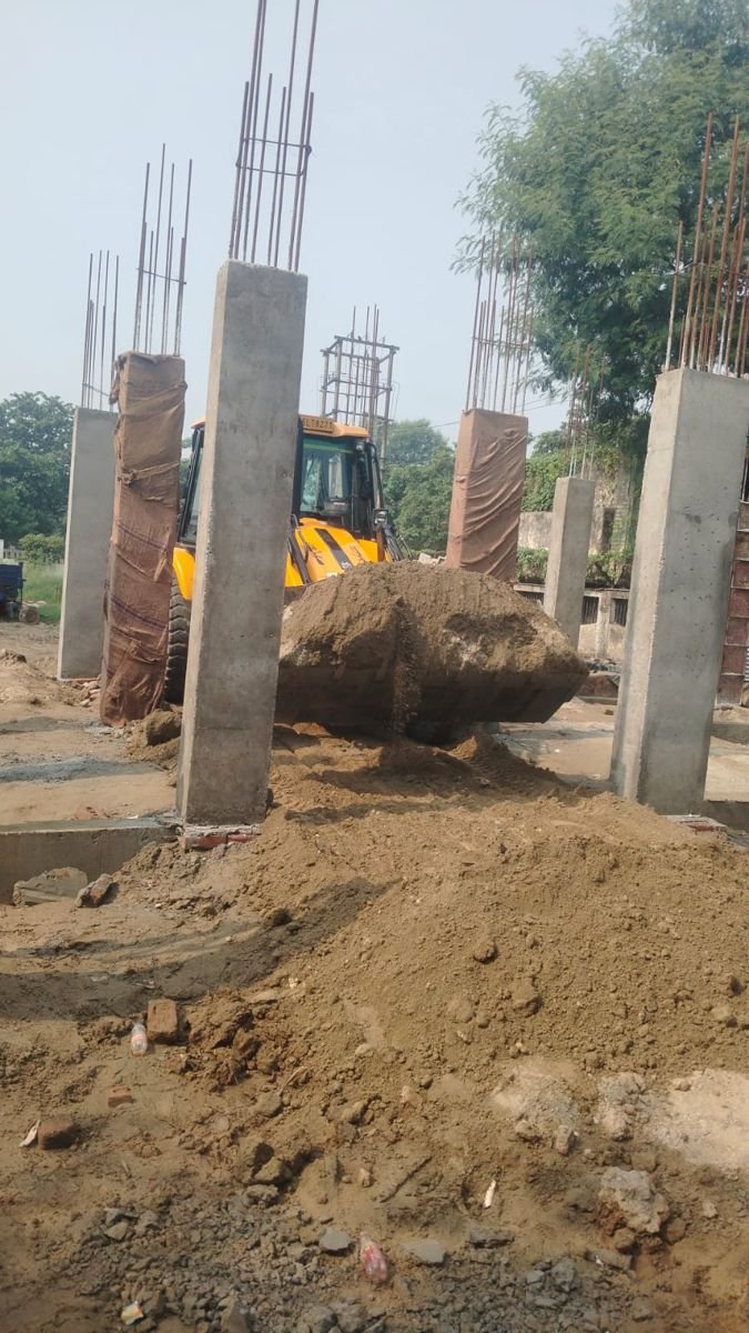 Fresh RCC columns at a construction project in Greater Noida, with a JCB backhoe moving soil around the site