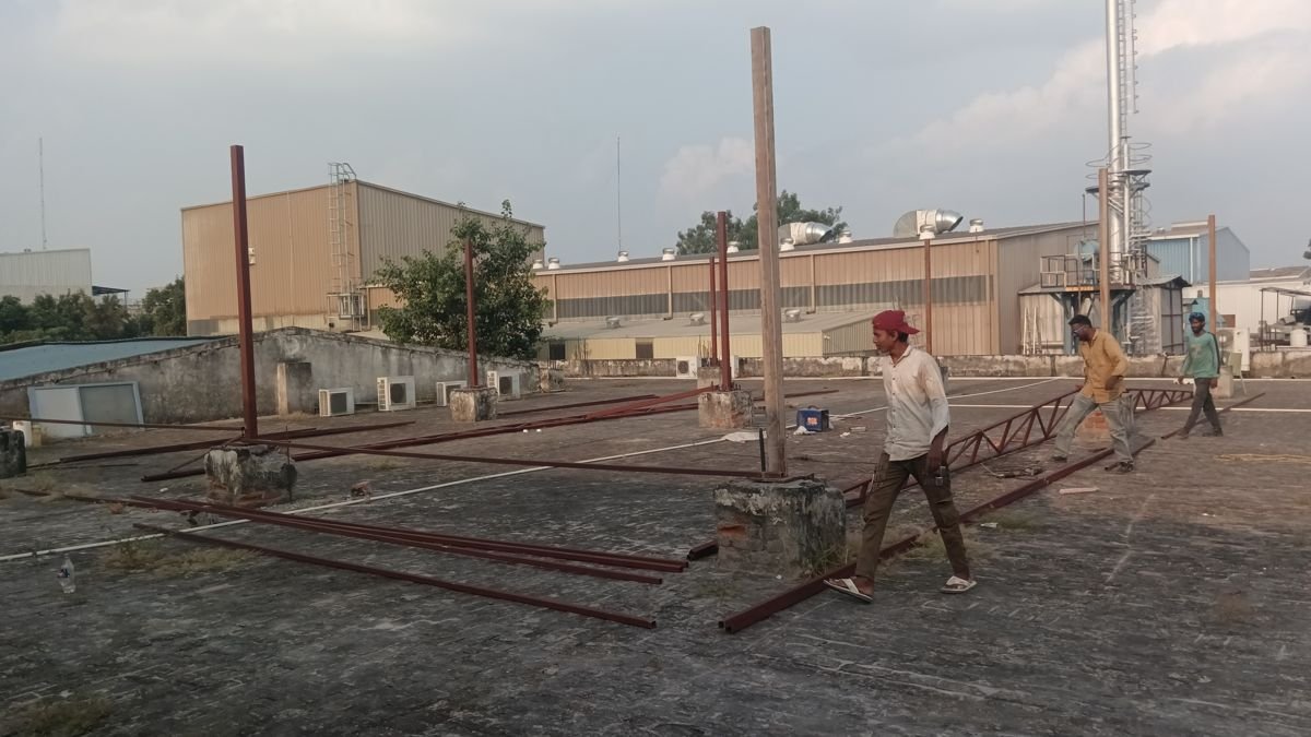 Steel columns and a lattice truss being laid out on a rooftop in Greater Noida