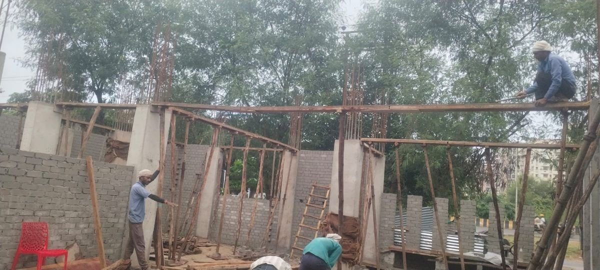 Brick walls rising between cast concrete columns at a construction site in Greater Noida, with timber and steel props be