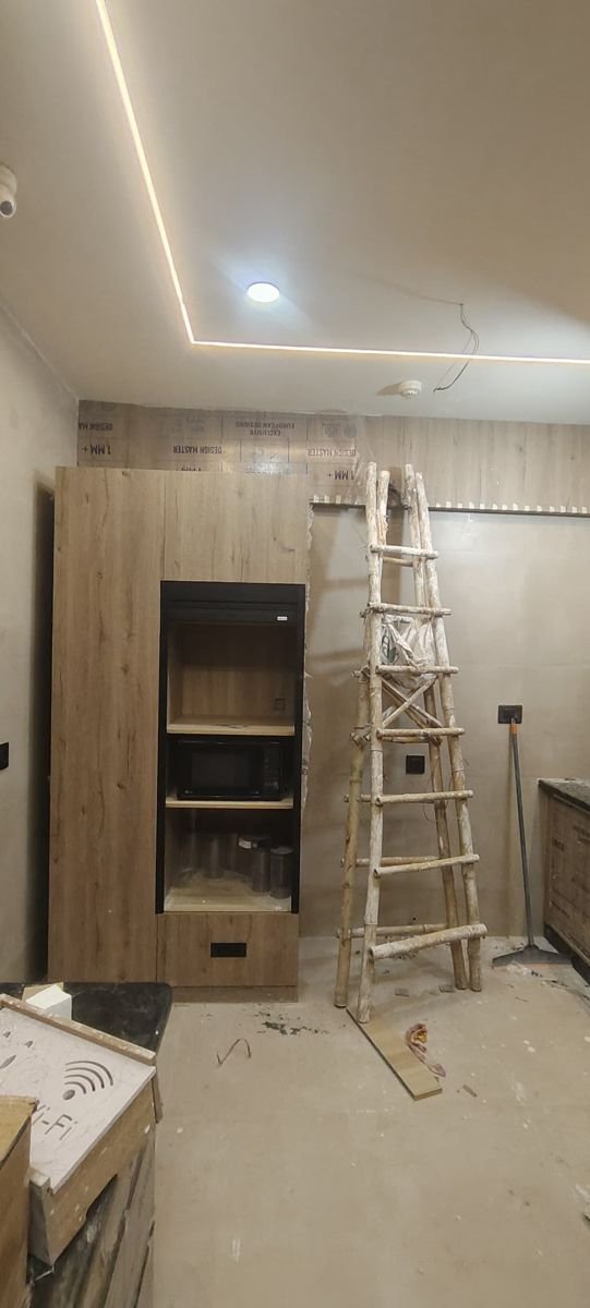 Tall kitchen unit in a wood-finish laminate with a built-in microwave niche and a drawer below, being installed at a hom
